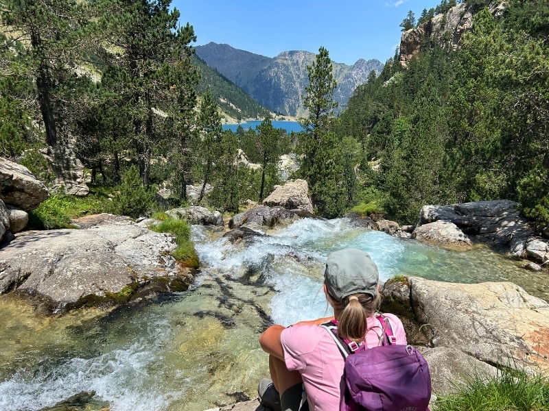 woman wearing a rucksack sitting on a rock above a waterfall and turquoise mountain lake