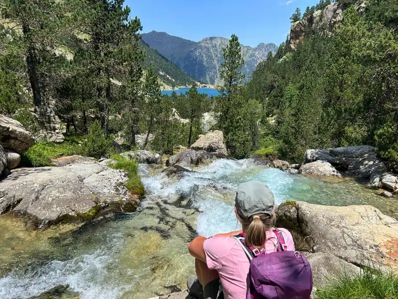 woman wearing a rucksack sitting on a rock above a waterfall and turquoise mountain lake