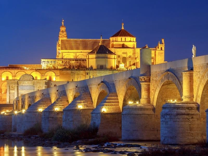 historic honey coloured building and Roman bridge lit up against the night sky