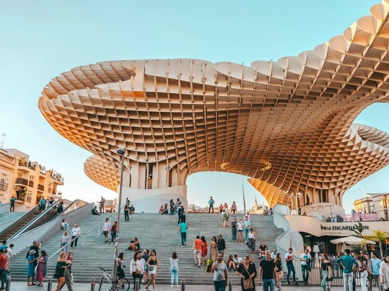 giant latticed wooden structure towering over people climbing concrete steps