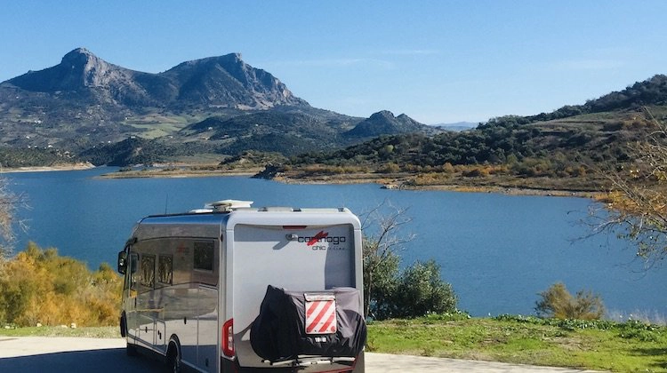 A parked motorhome overlooking a blue lake and mountains in Spain