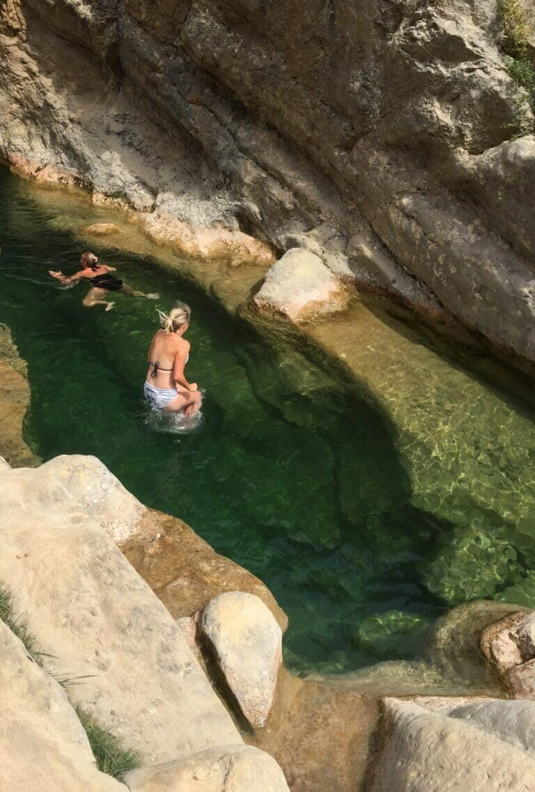 lady in a bikini jumping into a rocky pool of clear water