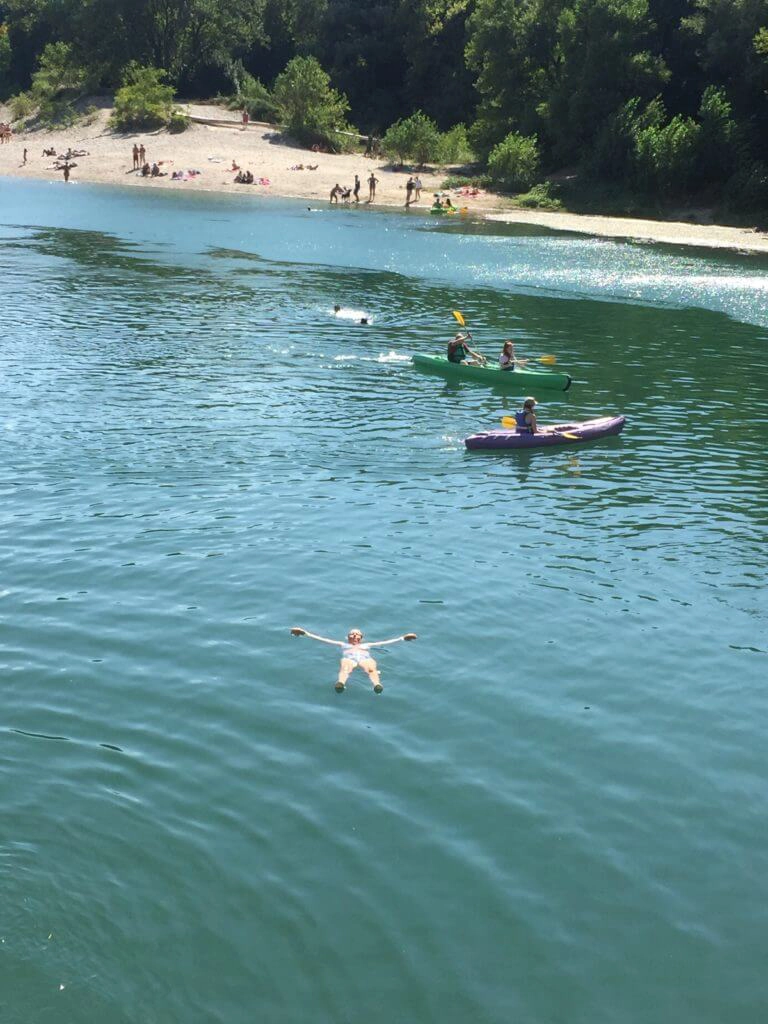 people swimming and canoing in a river with a beach