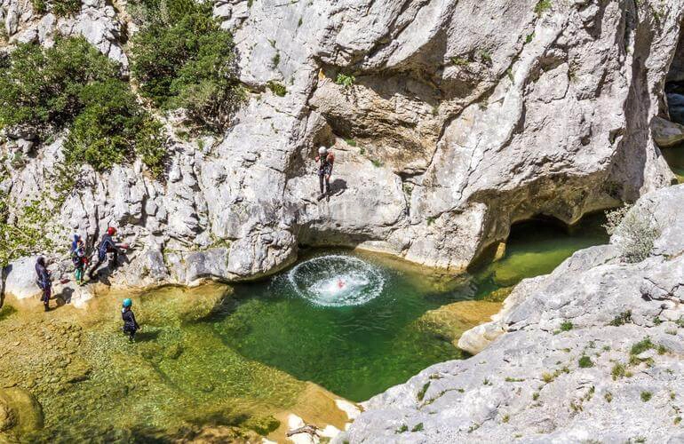 emerald pool surrounded by rocks with people wearing wetsuits and helmets