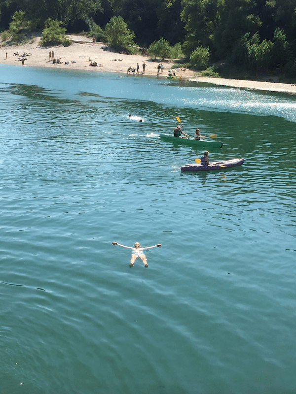 people swimming and canoing in a river with a beach