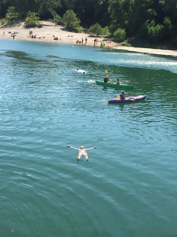 people swimming and canoing in a river with a beach