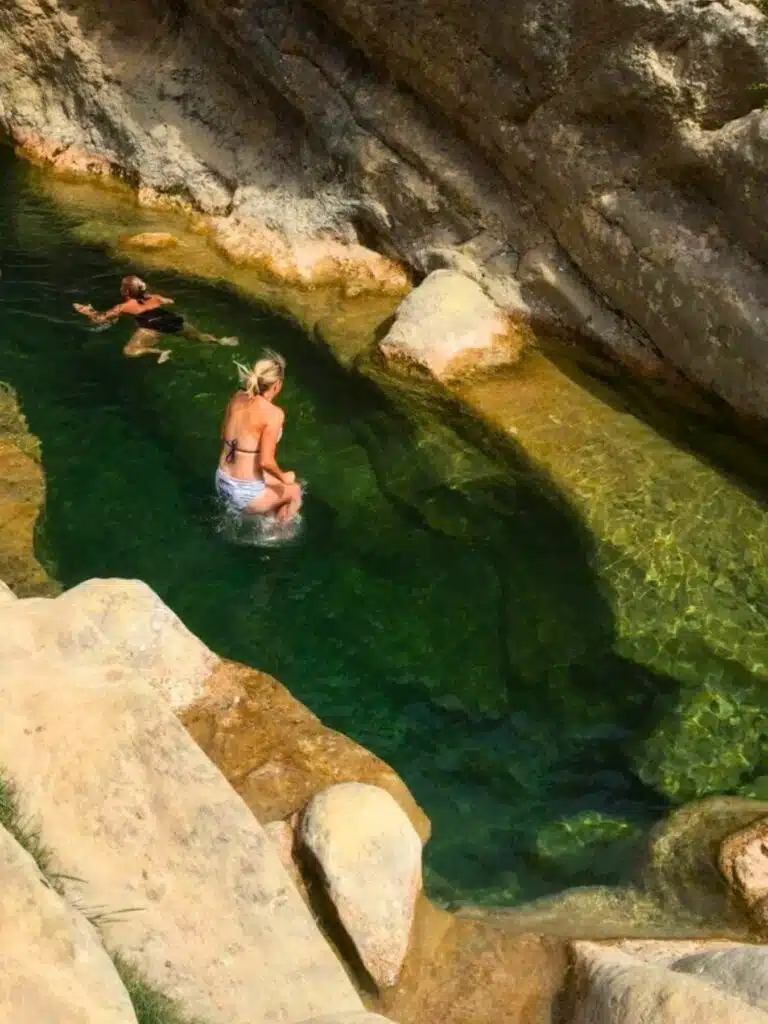lady in a bikini jumping into a rocky pool of clear water
