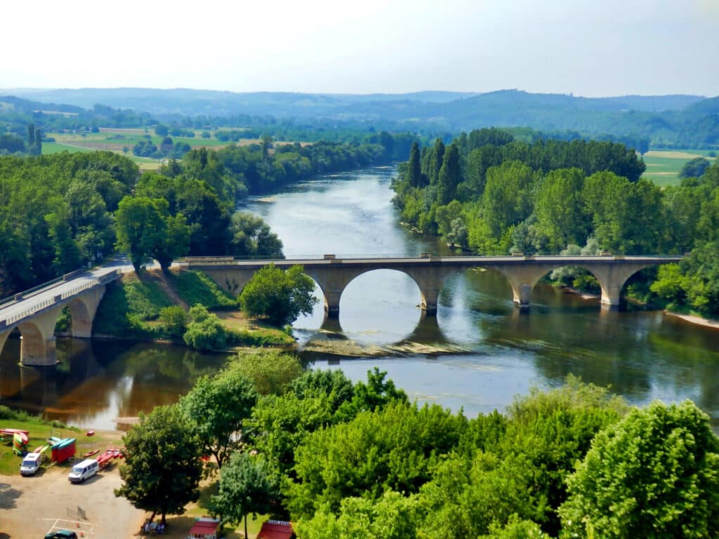 wide river flowing under an arched bridge and flanked by river beaches