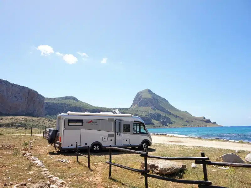 silver motorhome on a grassy beach with blue sea and a mountain in the distance