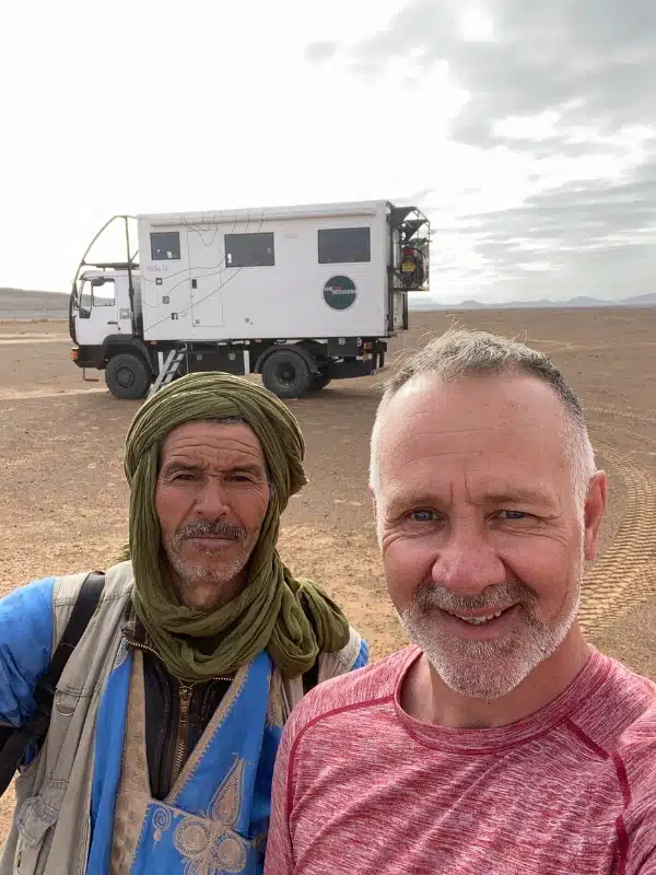 Two men in the desert in front oa a white overland truck