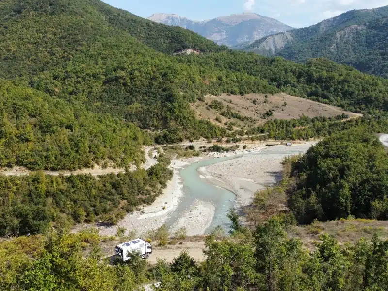 camper parked above a mulky green river surrouned by wooden mountains