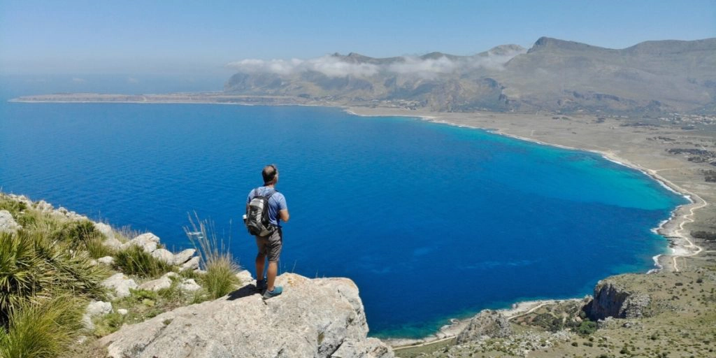 man standing on a rocky outcrop high above a deep blue sea and a huge bay