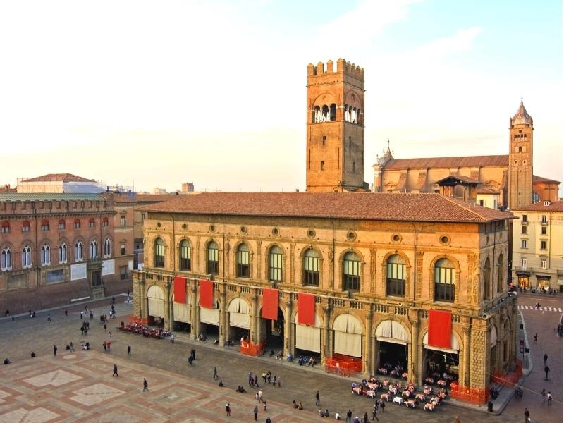 historic city building in stone with arched windows and a creneliated tower, in front of a grand sqare