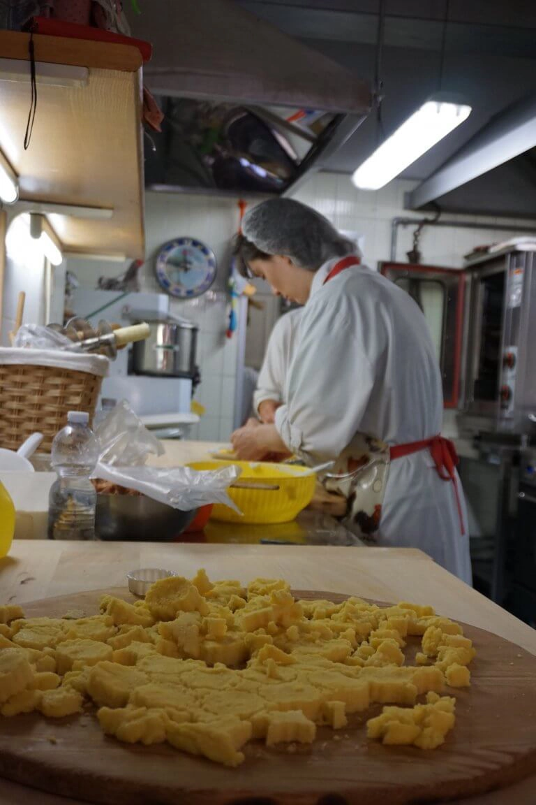 ladies in white coats and red hats making pasta by hand