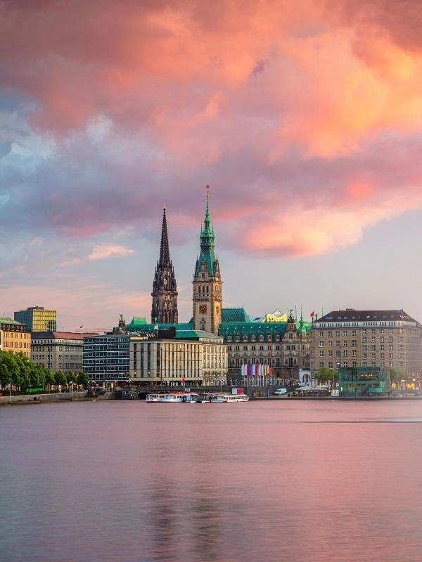 Hamburg's rathaus and St Nikolai spire across the Aussen-Alster against a pink cloudy sky
