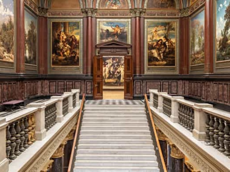 stairs into a musuem with wooden panelling and paintings on the walls