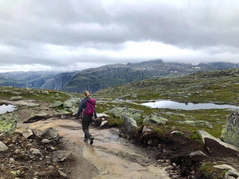 Woman wearing a pink rucksacj hiking across muddy and rocky terrain