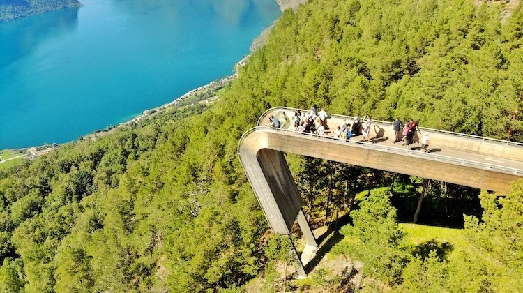 people on a metal viewpoint above a turquoise fjord 