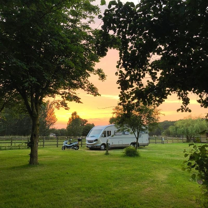 motorhome and scooter parked in a grassy meadow surrounded by trees at sunset
