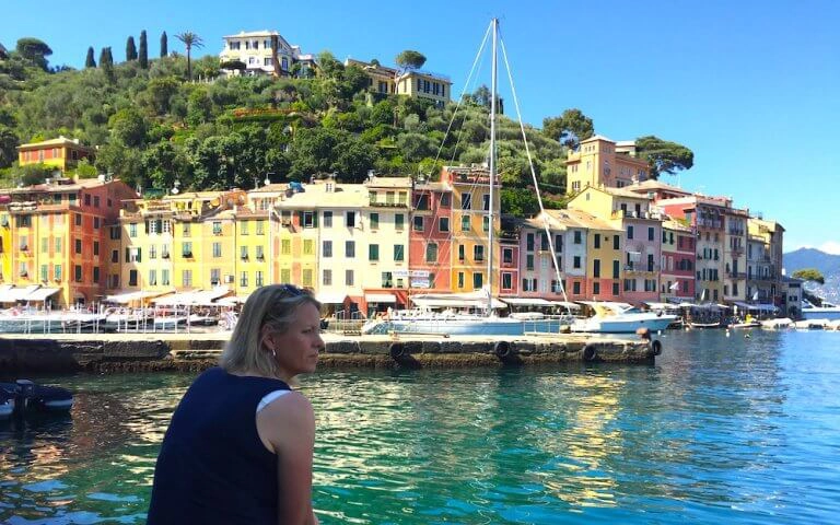 Woman sitting by a turquoise sea full of yachts with colourful houses in the background