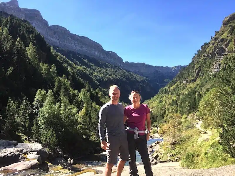 couple in hiking gear in front of a river with a wooden mountain backdropp