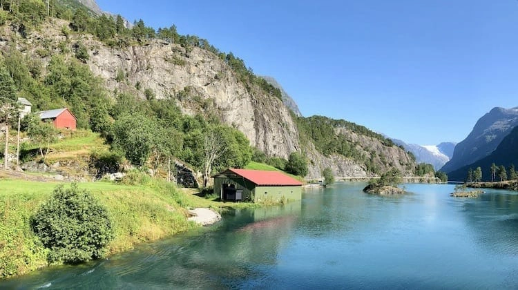 red and green shed by the edge of lake surrounded by mountains