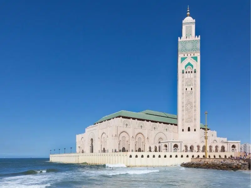 large white and green mosque with a tall minaret and the sea on one side