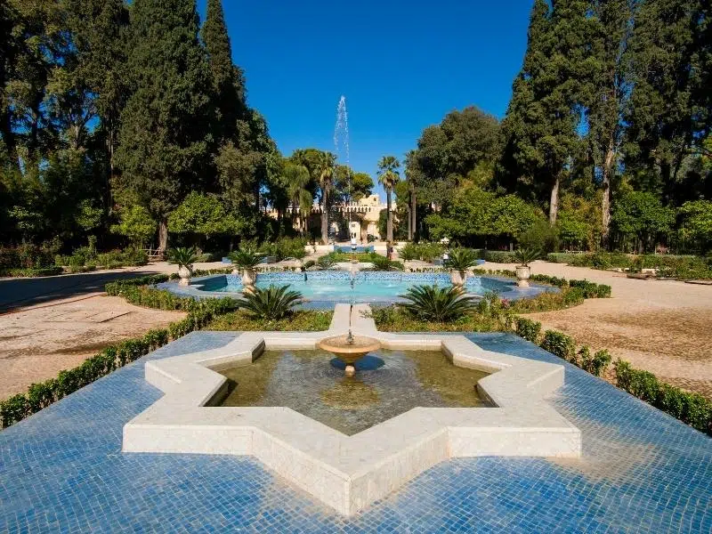 star shaped fountain in symmetrical garden with palace in the background and trees om either side