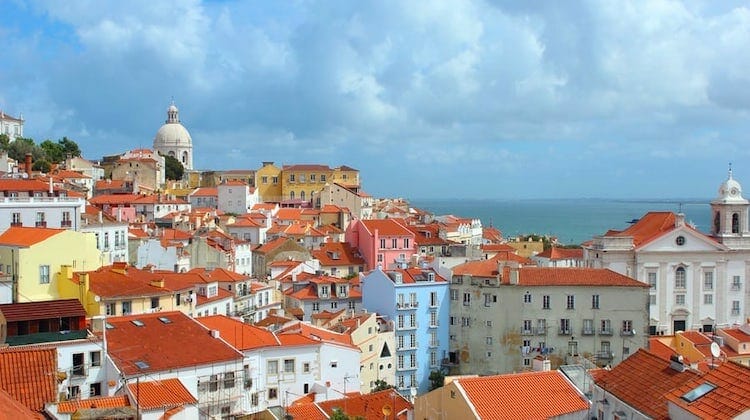 red roofed colourful houses and domed topped church in front of sea and cloudy sky