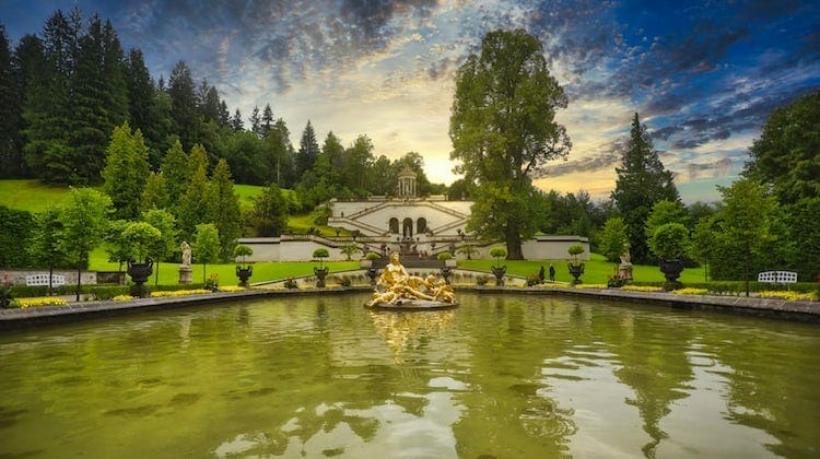 pond with golden statue in front of ornate stairs, surrounded by grass and trees