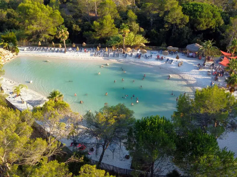 Areal shot of a natural pool surrouned by sand, trees and sun loungers