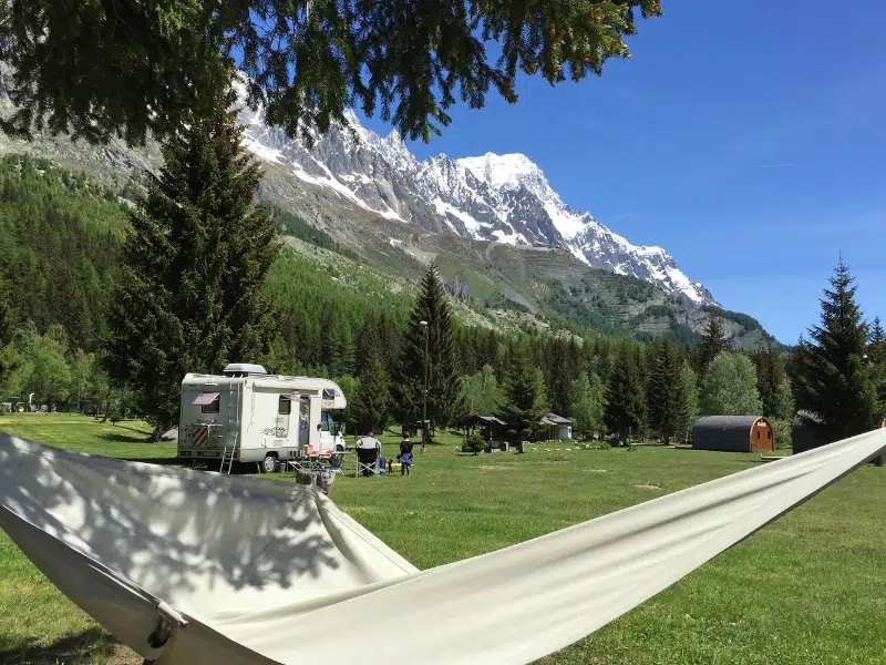 Hammock and a motorhome parked in a grassy field with a large snowy mountain backdrop