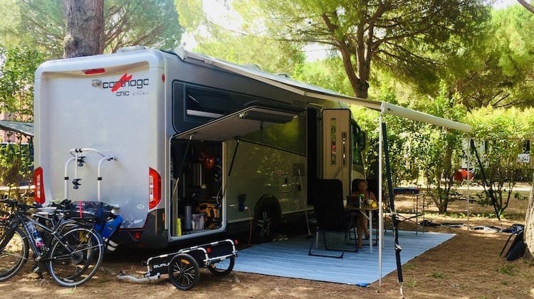 silver motorhome with awning out surrounding by camping equipment and bikes