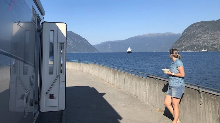 Person standing by a motorhome looking out across a fjord to a boat