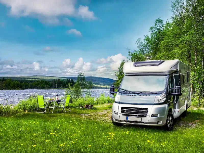 white motorhome by a river with green fold up chairs outside
