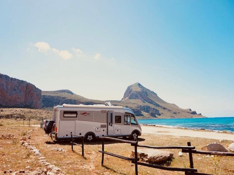 motorhome parked on the beach by blue sea and mountains