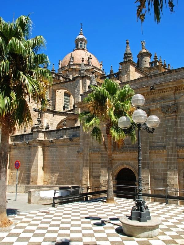 Large creamy stone church with domed roof and palm trees in the foreground