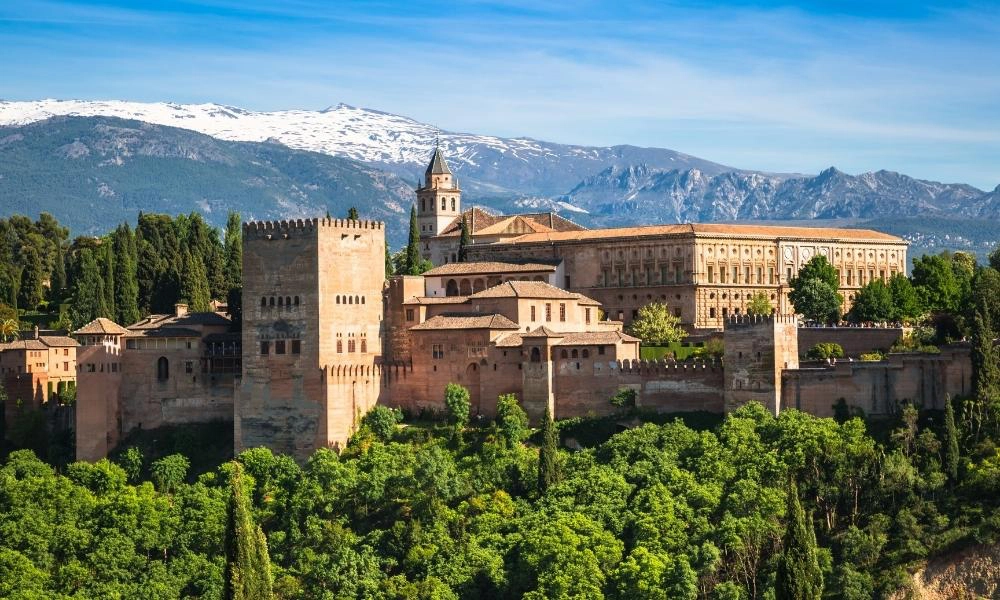 moorish castle amongst green tress with snow capped mountains behind