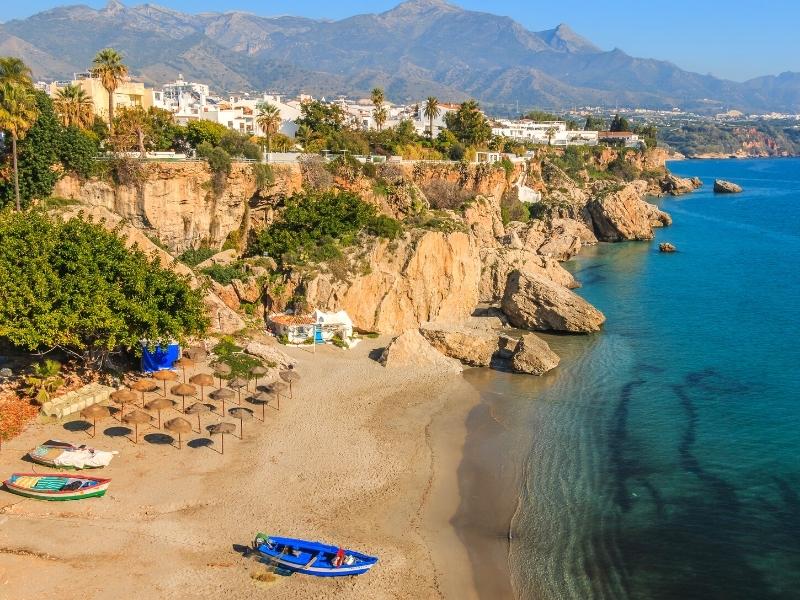 sandy beach with rock, clear sea and a white village on the cliffas above