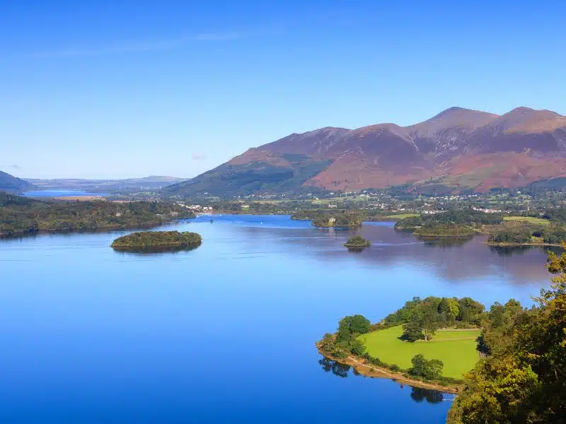 A view across Derwentwater in the English Lake District National Park to the town of Keswick and beyond is Skiddaw.