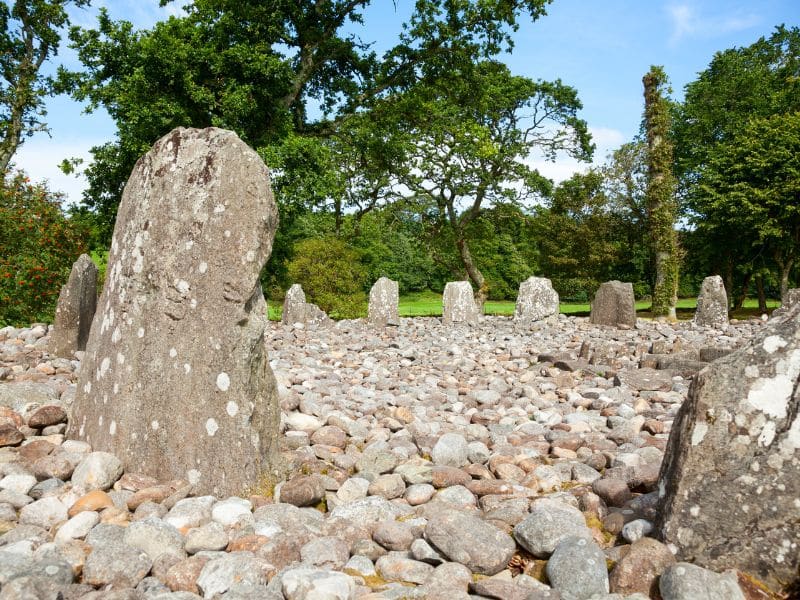 Circle of standing stones filled with pebbles and surrounded by grass and trees