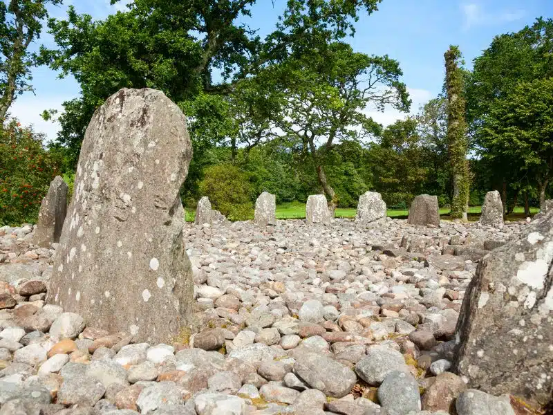 Circle of standing stones filled with pebbles and surrounded by grass and trees