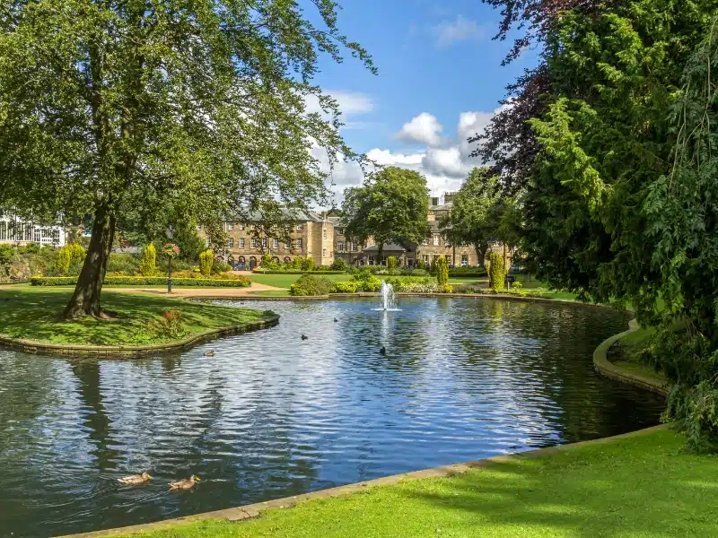 Lush gardens with a small lake and historic buildings in the background