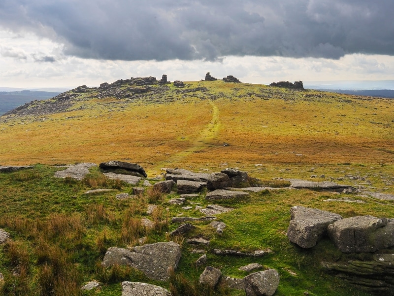 Looking up to Great Staple Tor from Roos Tor under dark cloudy sky, Dartmoor National Park, Devon, UK