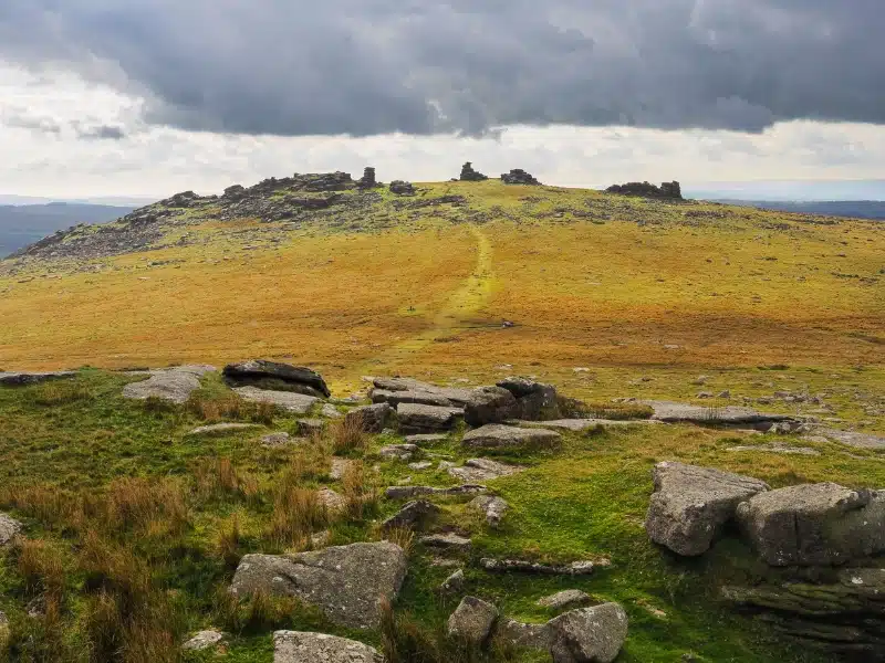 Looking up to Great Staple Tor from Roos Tor under dark cloudy sky, Dartmoor National Park, Devon, UK