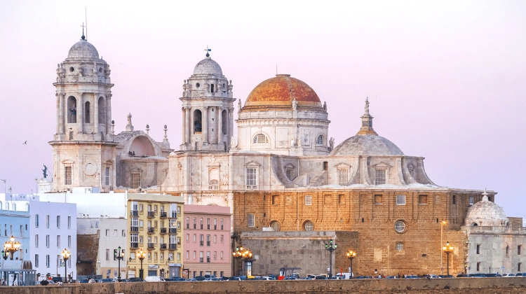 The cathedral of Cadiz Spain with orange and pink walls and an orange dome, against a pinky winter sky