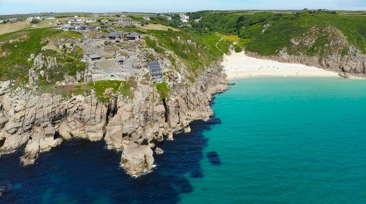 small sandy cove and turquoise water with a theatre on rocky cliffs 