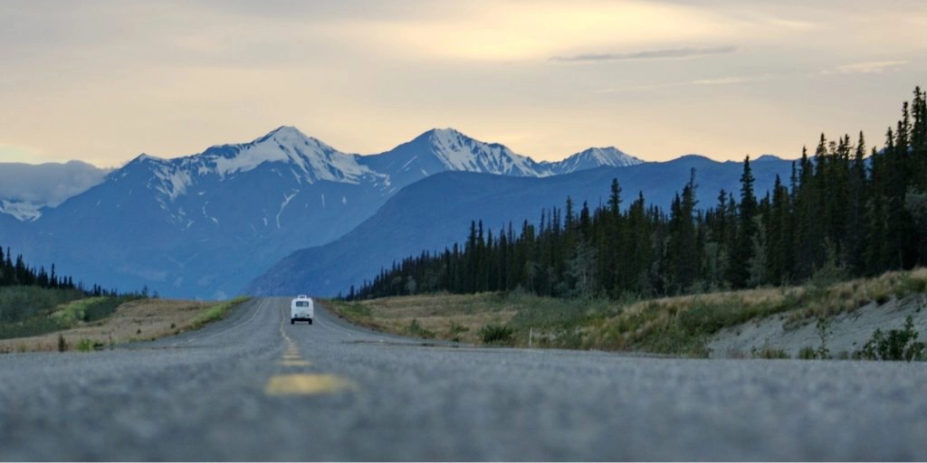 white campervan on a great road with pine trees and mountains surrounding the road