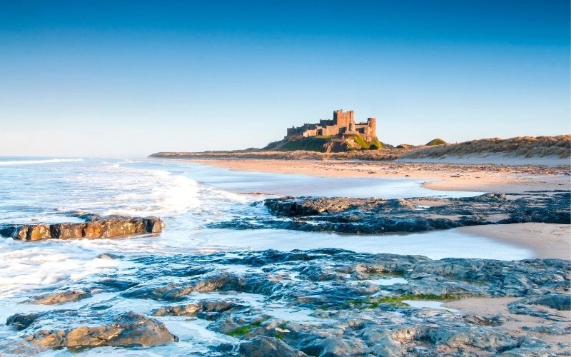 large castle standing next to a sandy beach with rocks in the water