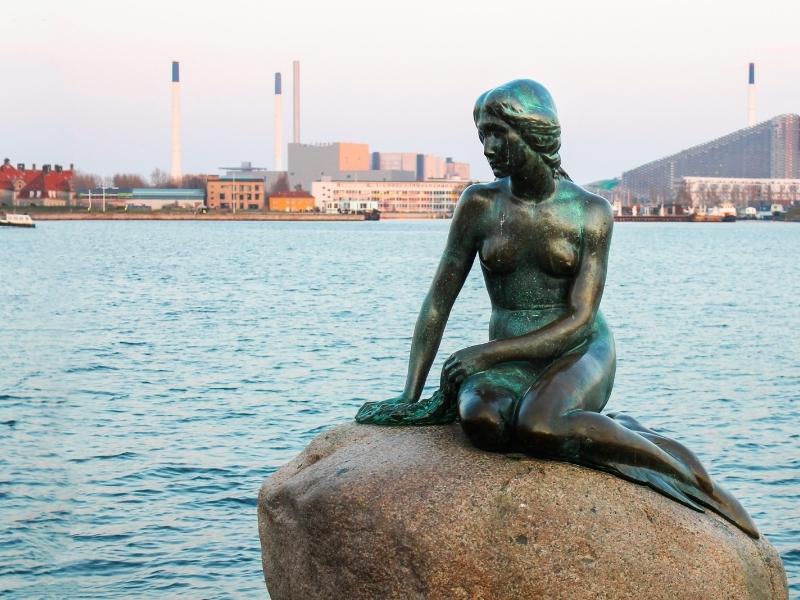 small bronze startue of the little mermaid with Copenhagen city behind